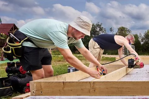Construction workers assemble timber floor frame, one measuring wooden beam.. Stock Photos