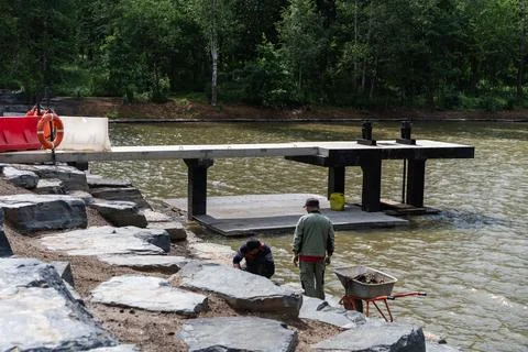 Construction workers assembling modular pier on woodland lake Stock Photos
