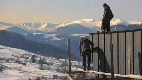 Construction workers assembling a rooftop against a stunning backdrop of snow Stock Footage 304049680