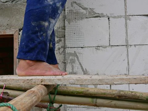 Construction worker's bare feet standing on a wood plank on bamboo scaffolds Stock Photos