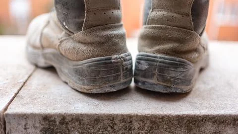 Construction worker's boots full of dirt, on a stone tile. Stock Photos
