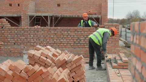 Construction workers building brick wall. Two construction workers in safety Stock Footage 301557564