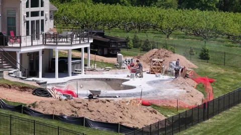 Construction workers building freeform luxury pool beside two-story home with Stock Footage 336460761