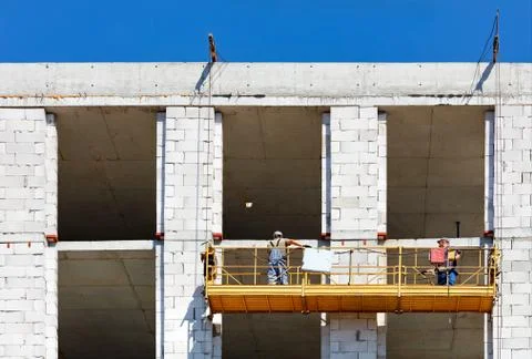 Construction workers climb on a cradle along the facade of a building under c Stock Photos