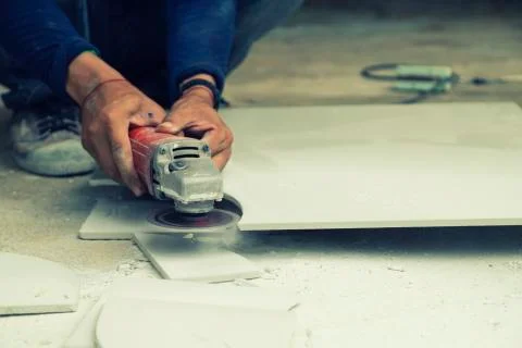 Construction workers cut the tiles into the shape with electric tile cutter w Stock Photos