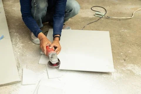 Construction workers cut the tiles into the shape with electric tile cutter w Stock Photos