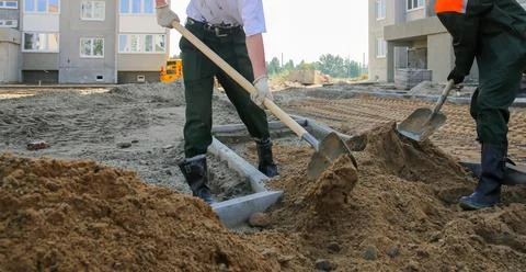 Construction workers dig at a construction site in daylight near new buildi.. Stock Photos