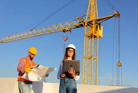 Construction workers discussing blueprint on building site with crane Stock Photos