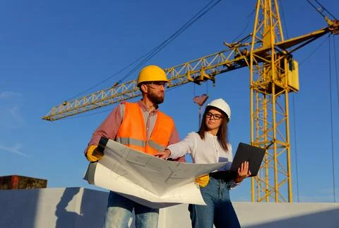 Construction workers discussing blueprint on building site with crane Stock Photos