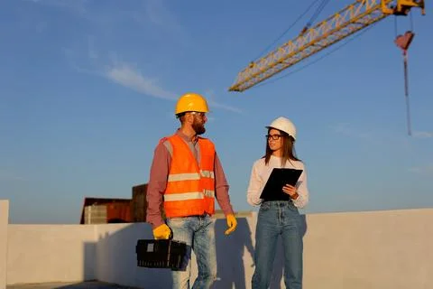 Construction workers discussing blueprint on building site with crane in ba.. Stock Photos