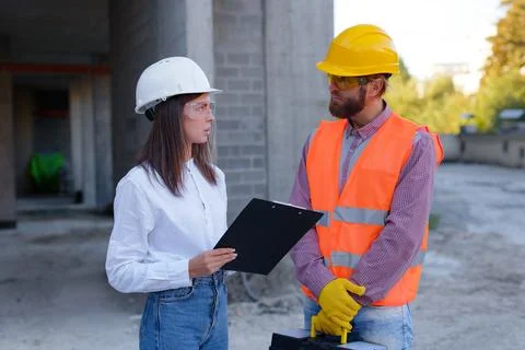Construction workers discussing blueprint on clipboard at construction site Stock Photos