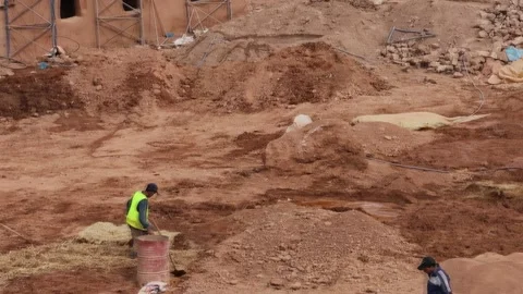 Construction workers excavating and moving soil at a dusty desert worksite. Stock Footage 336536694