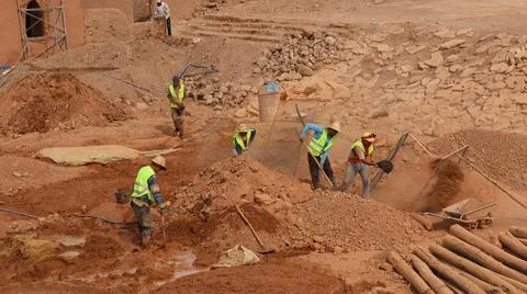 Construction workers excavating and moving soil at a dusty desert worksite. Stock-Fotos
