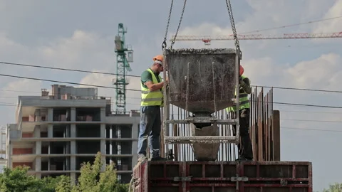 Construction workers guide concrete hopper above reinforced formwork at active Stock Footage 346604045