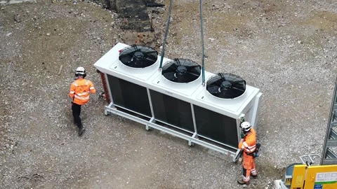 Construction workers guide industrial cooling unit as helicopter performs Stock Footage 336461900