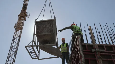 Construction workers guide a suspended concrete hopper beside tall formwork 動画素材 340030035