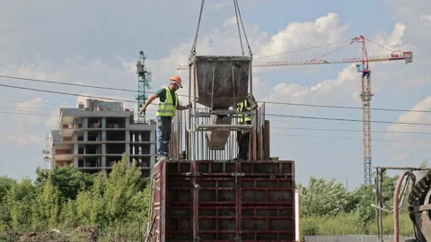 Construction workers guide suspended concrete hopper above reinforced formwork Видео 343407722