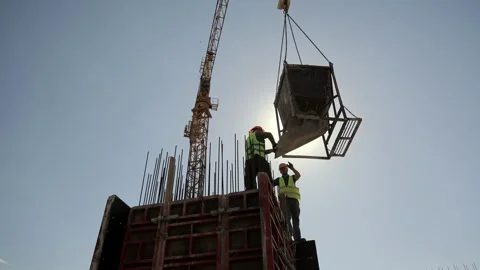 Construction workers guide suspended concrete hopper above reinforced formwork Stock Footage 343411452