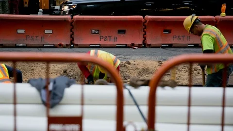 Construction workers in harhats shoveling dirt behind safety barrier NYC Stock Footage 99091563