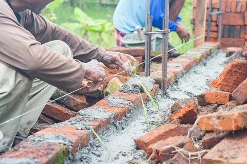 Construction workers install bricks and cement from rows of bricks on exterio Stock Photos