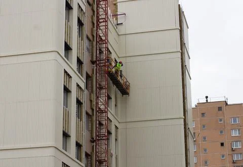 Construction workers install insulation and siding on a new urban home using a Stock Photos