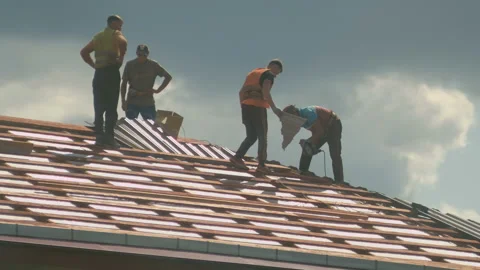 Construction workers install a new metal roof tile on a house Stock Footage 130260199