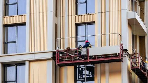 Construction workers installing facade elements on suspended platform Stock Photos