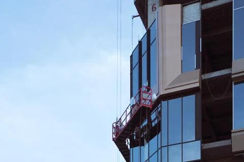 Construction workers installing glass panels from suspended scaffolding 스톡 사진