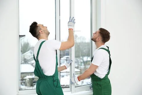 Construction workers installing plastic window in house Stock Photos