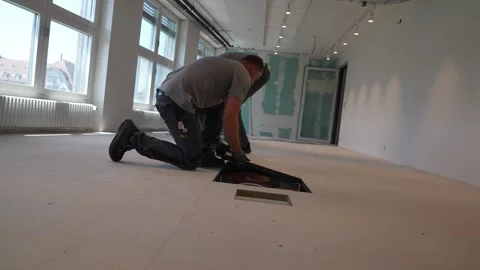 Construction workers kneeling on subfloor install raised floor panel and manage Stock Footage 331305172