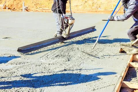 Construction workers leveling fresh concrete on building site during work day Stockfoto's