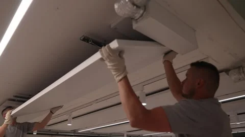 Construction workers lift and attach a large ceiling panel inside a modern 動画素材 331304577