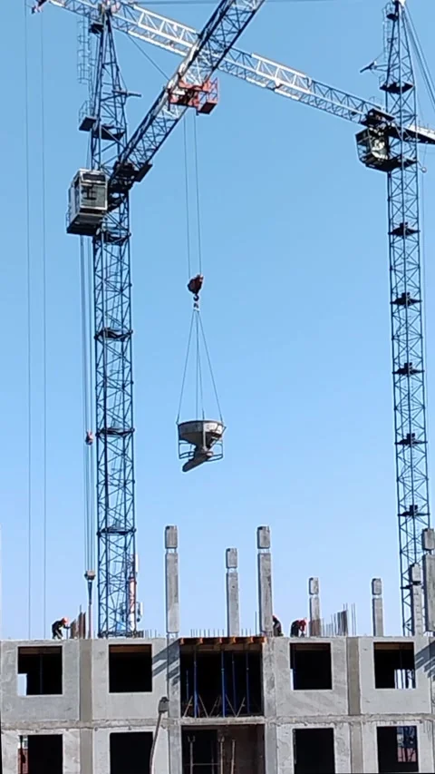 Construction workers operate cranes to lift concrete block onto building Stock Footage 340606801