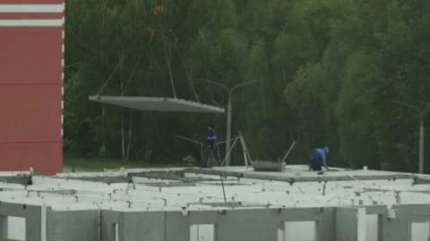 Construction workers oversee movement of large concrete slab by crane for Stock Footage 339865812