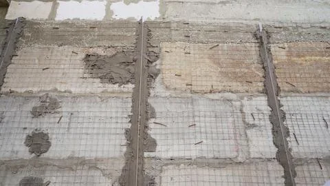 Construction workers plastering concrete wall with wire mesh reinforcement Foto stock
