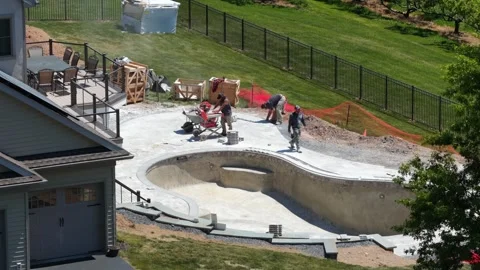Construction workers pouring concrete for luxury pool with curved shell beside Stock Footage 336460265