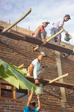 Construction workers reach out to each other lifting cement buckets up for ca Stock Photos