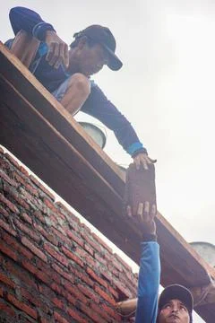 Construction workers reach out to each other lifting bricks up to build a wal Stock Photos