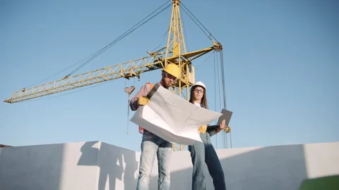 Construction workers reviewing plans under a crane in a sunny outdoor setting Stock Footage 295956875