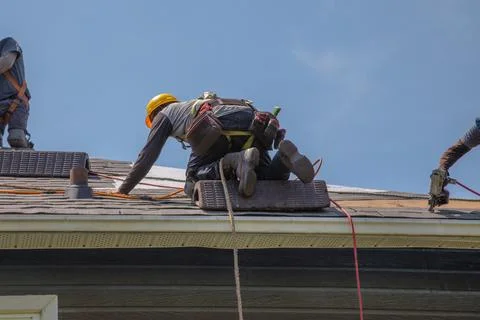 Construction Workers with Safety Equipment Installing Asphalt Shingles on R.. Stock Photos