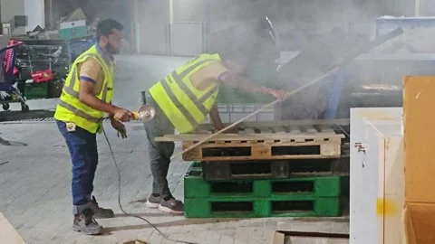 Construction workers in safety vests cut a wood sheet outdoors on pallets amidst Stock Footage 338259091