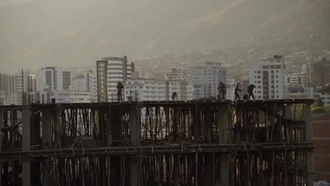 Construction Workers Silhouetted on Building Structure with City Background Stockbeeldmateriaal 310406456