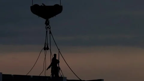 Construction workers silhouettes against evening sky during sunset, crane hook Stock Footage 325298296