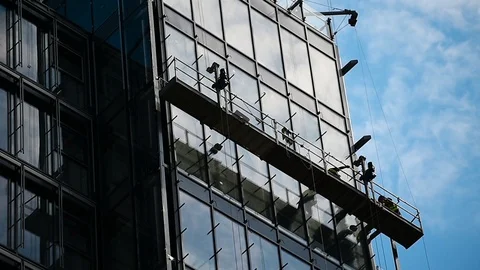 Construction workers on a suspended platform on a skyscraper glass facade Video stock 93180203