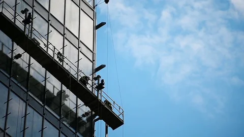 Construction workers on a suspended platform on a skyscraper glass facade 스톡 동영상 93180213