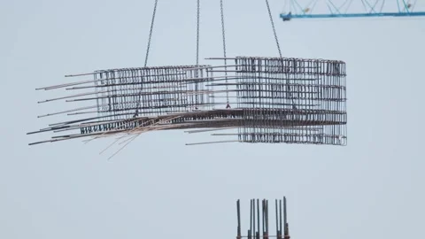 Construction workers use a crane to lift metal rods at a building site in the Vídeos de archivo 338246199