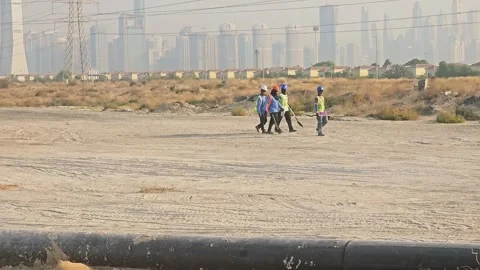 Construction workers walking across an open, sandy plot of land at a dusty Vídeos de archivo 338308260