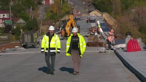Construction workers in work jackets walk along the road along the construction Stock Footage 292880241