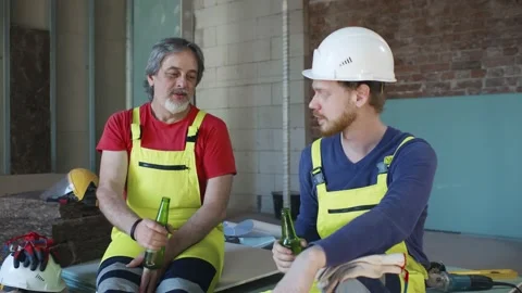 Construction workers in work wear, helmets drink beer from bottle at work 스톡 동영상 133635688