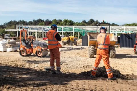 Construction workers working on building site with industrial units. Stock Photos